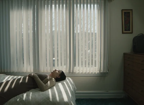 A woman lying on a bed beneath bands of window light